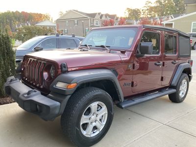 Maroon Jeep Wrangler with four doors and a black soft top sitting in a driveway.