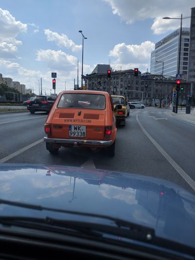 View from a car of a 1988 orange Yugo.