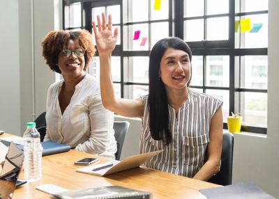Woman sitting and raising her hand beside another woman.