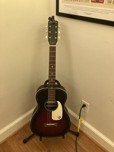 A Gretsch parlor acoustic guitar with a sunburst pattern on the top and a white pickguard.