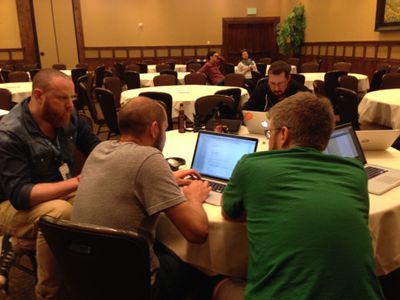 Four people huddled around laptops, sitting at a table, working late on a project.