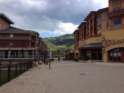 Shops and restaurants inside Canyons Resort in front of a mountainous backdrop.