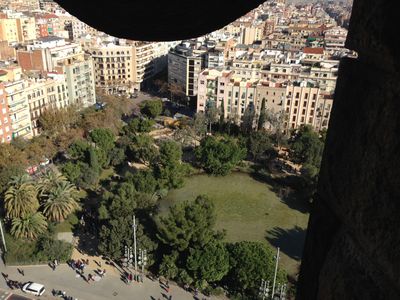 A view of Barcelona from atop La Sagrada Familia, an ornate church in Barcelona, Spain. It shows a grassy field below, surrounding by trees.