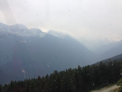 The fog sets in on a mountain, on one of the peaks while trees line a forest below.