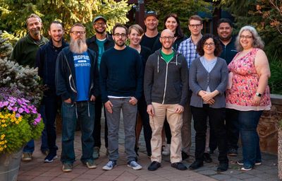 Group photo of the Automatic Theme Team, 13 people standing in front of trees smiling.