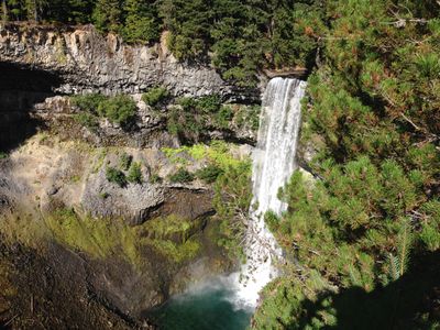 Brandywine Falls, near Whistler, British Columbia. A waterfall pours down the side of a cliff high up amid a forest of trees.