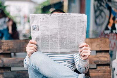 Man sitting on bench reading newspaper.