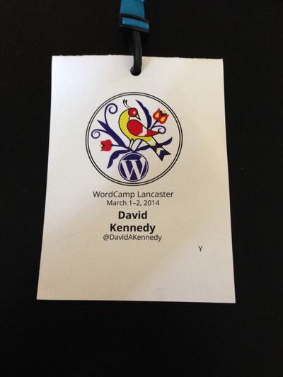 Conference badge with a blue, yellow and red bird in the center followed by the WordPress logo. Includes: WordCamp Lancaster, March 1-2, 2014; David A. Kennedy, WordCamp Lancaster 2014 conference badge.